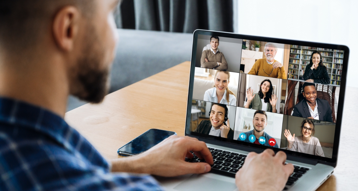 This image showcases a man sitting down in front of his laptop having a virtual meting which has several attendees